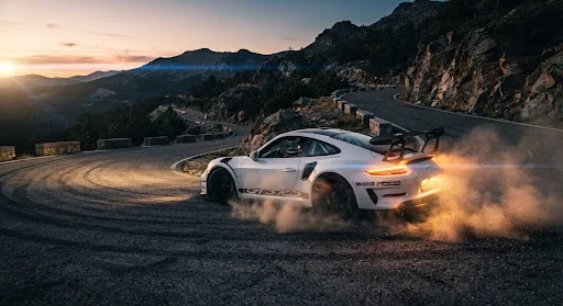 Porsche 911 GT3 RS drifting violently through high mountain hairpin turns in the Sierra Nevada at golden dusk, dramatic dust clouds illuminated by amber taillights, crisp anamorphic flare, motion blur on wheels, shot on ARRI Alexa 35 cinema camera