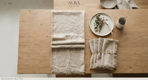 Overhead aesthetic flat-lay of folded oatmeal washed Belgian linen table runner and matching set of four napkins, raw fringed edges, minimalist wooden table setting, natural diffused earthy tones.