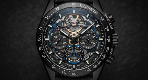 High precision black DLC skeleton chronograph watch face on a dark graphite background. Visible exposed column wheel movement, gold balance spring, and precision machined matte carbon fiber sub-dials. Razor sharp industrial lighting with warm brass reflections.