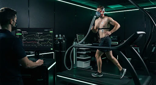 A focused male athlete undergoing VO2 max treadmill diagnostics wearing a clinical oxygen metabolic mask and physiological monitors inside a high-tech dark carbon sports performance laboratory with subtle neon green backlighting.