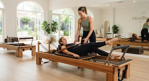 Polished timber custom Reformer carriage in a spacious sanctuary studio with mirrored walls, leather straps, and an athletic instructor guiding focused low-impact core alignment.