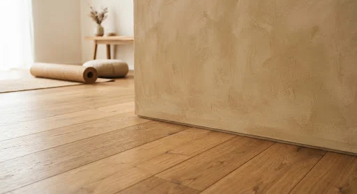 Close up architectural detail of warm heated European white oak floorboards meeting textured sand-toned lime wash walls in an ultra-peaceful studio.